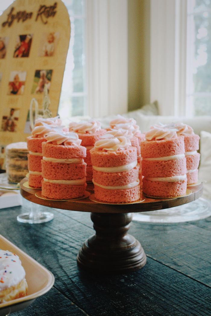 Pink mini sponge cakes with cream filling on a wooden cake stand.