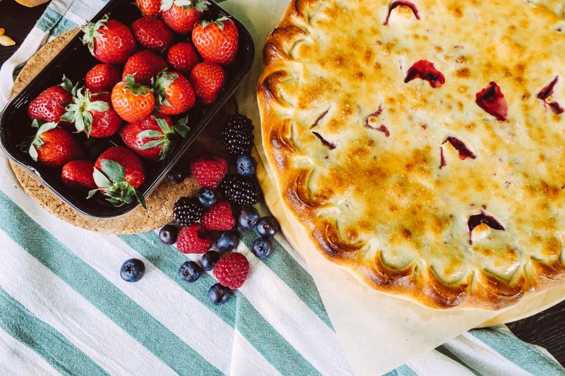 A golden homemade fruit pie surrounded by fresh berries.